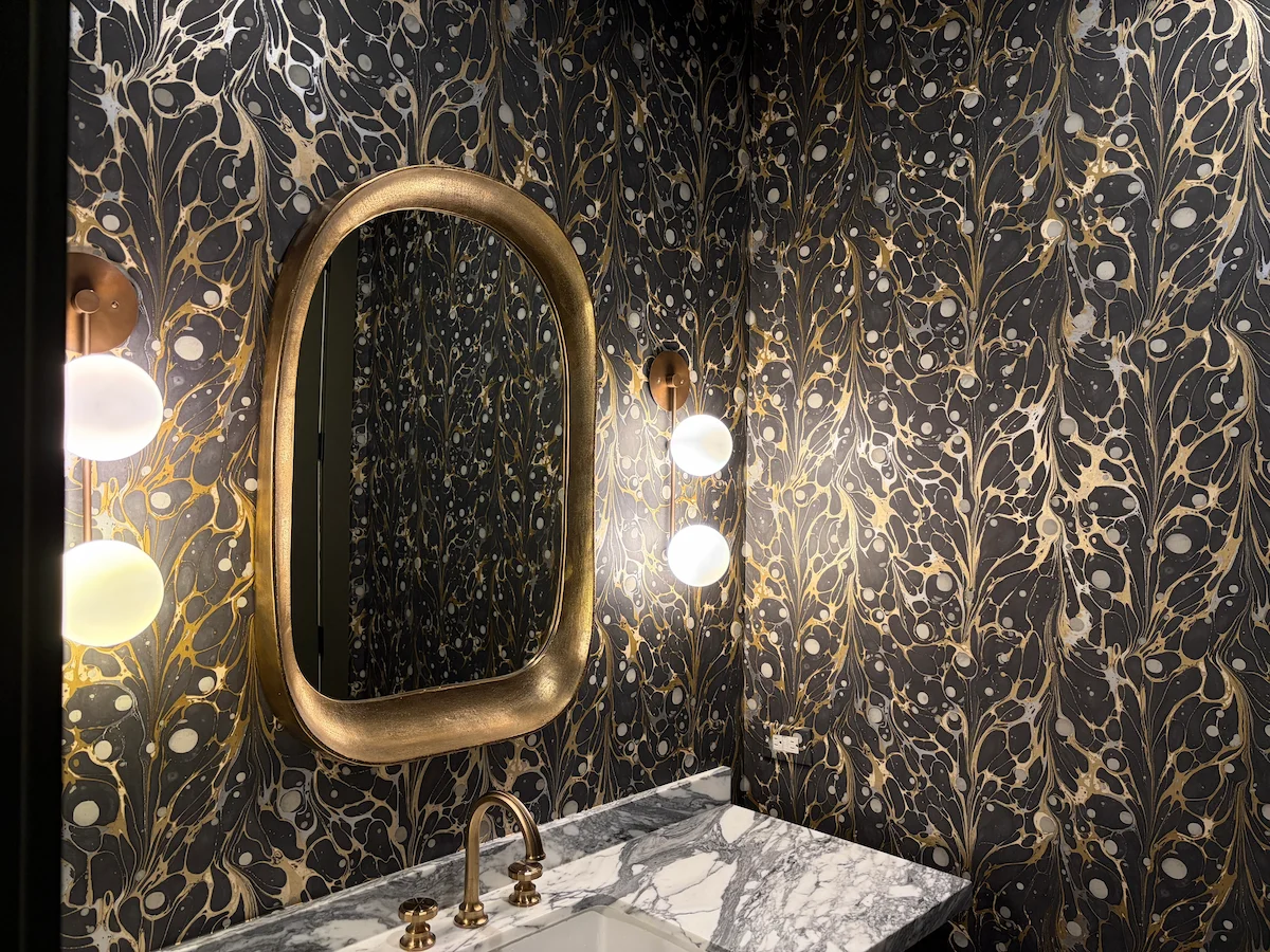 Dark botanical bathroom wallpaper paired with a gold framed mirror