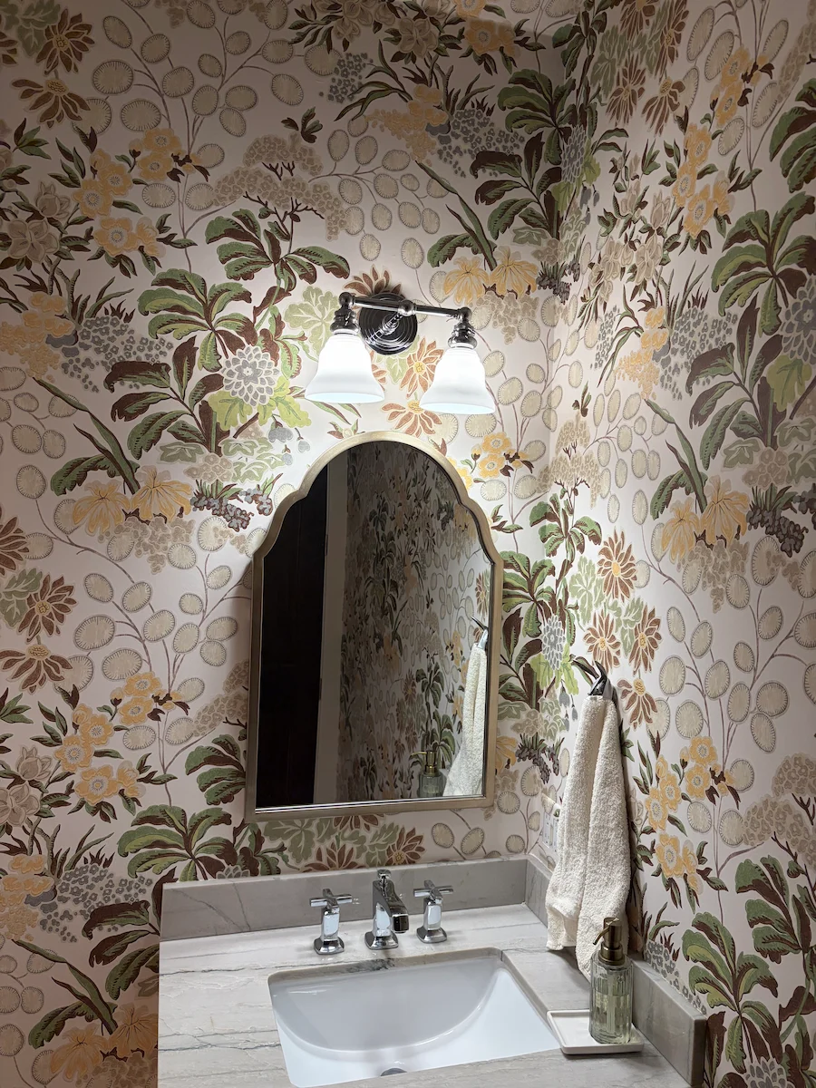 Floral wallpaper surrounding a powder room mirror and pedestal sink