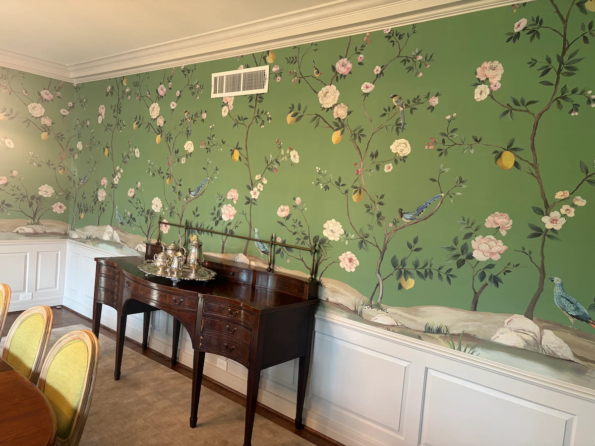 Green floral and bird wallpaper above white dining room wainscoting
